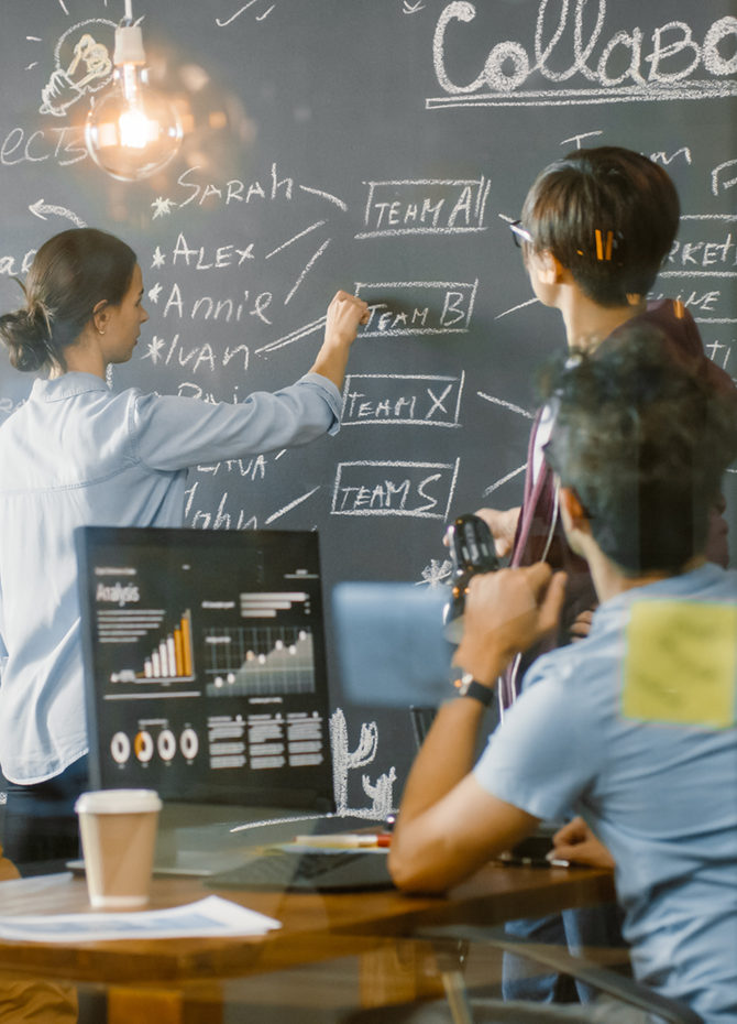 A team of professionals collaborating in a modern workspace, brainstorming ideas on a chalkboard to develop cooperation strategies and strategic partnership plans.