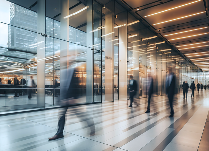 Business professionals moving through a modern corporate lobby in a glass office building.