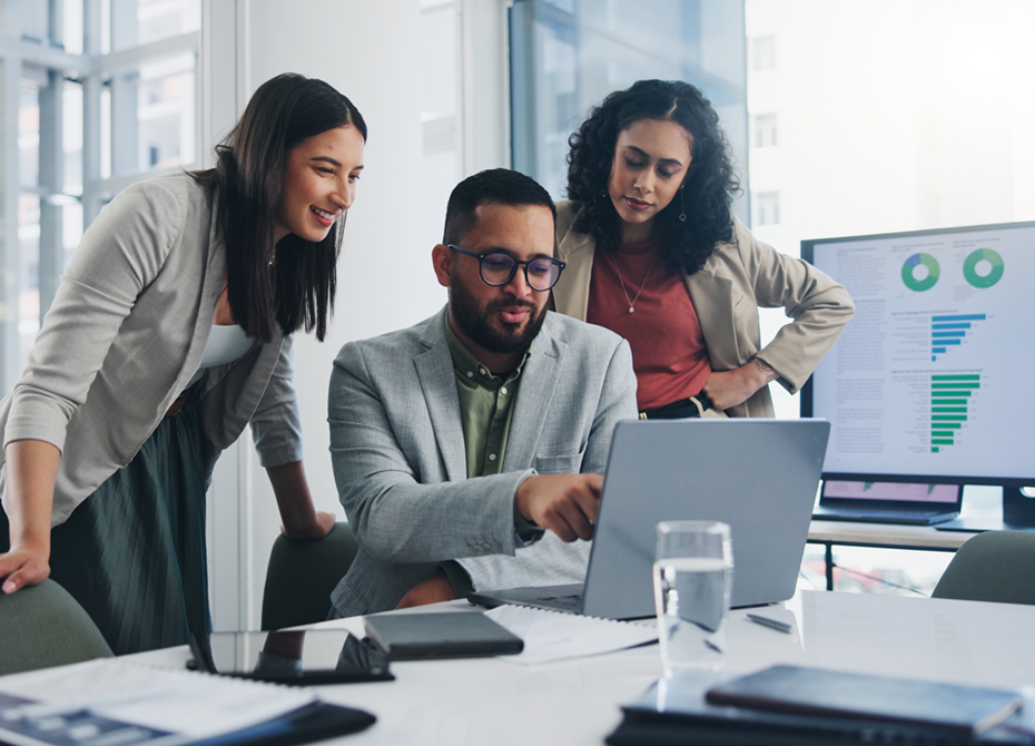 Team collaboration meeting showcasing professionals discussing data on a laptop and charts on a monitor, representing a modern office environment with personnel leasing services enabling flexible workforce solutions.
