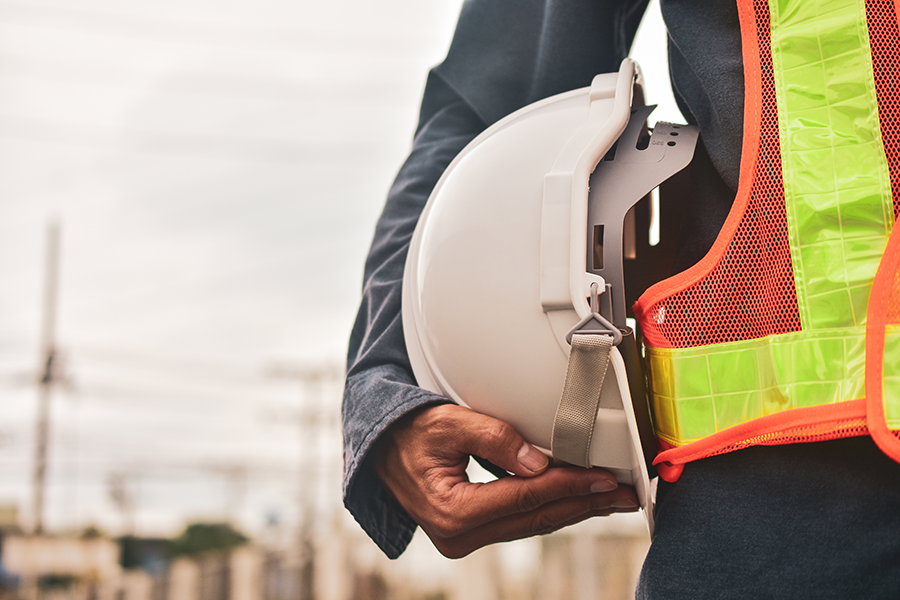 Close-up of a construction worker holding a safety helmet and wearing a high-visibility vest, highlighting the importance of workplace safety in industrial environments.