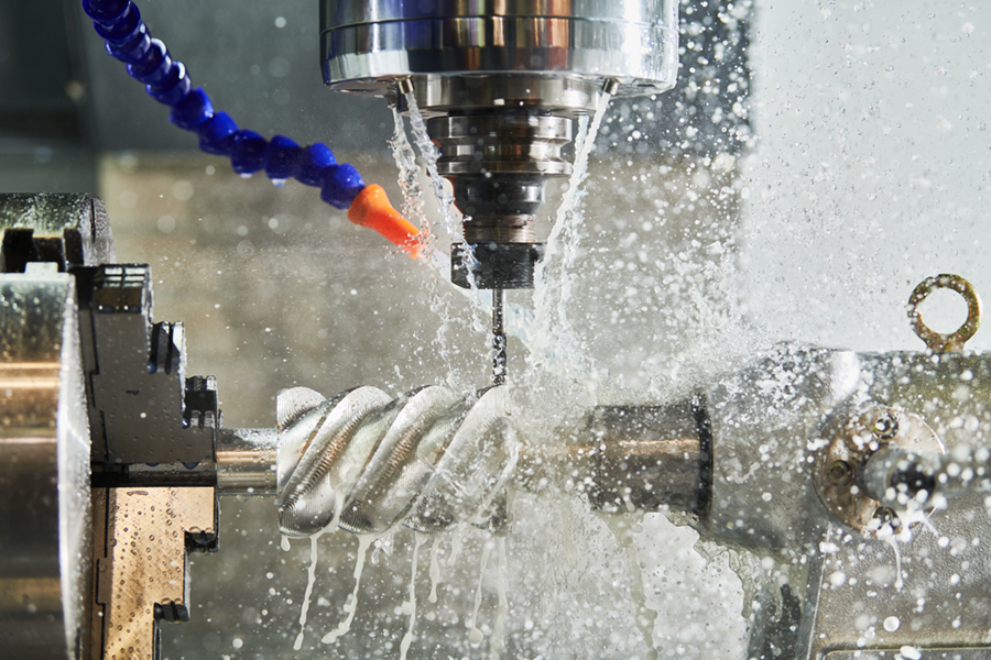 Close-up of a CNC milling machine cutting a metal workpiece with cooling lubricant being sprayed during the process.