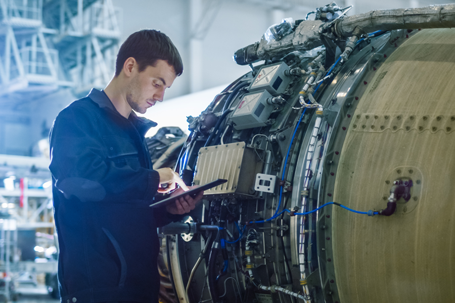 Engineer working on a tablet beside an aviation engine in an industrial setting.