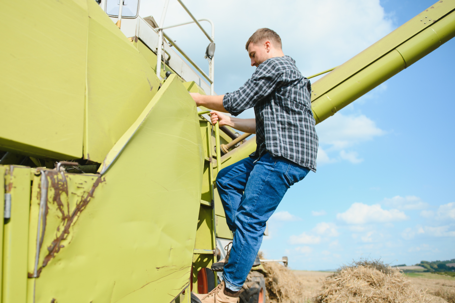 Man climbing onto a large piece of agricultural machinery in a rural field under a blue sky.