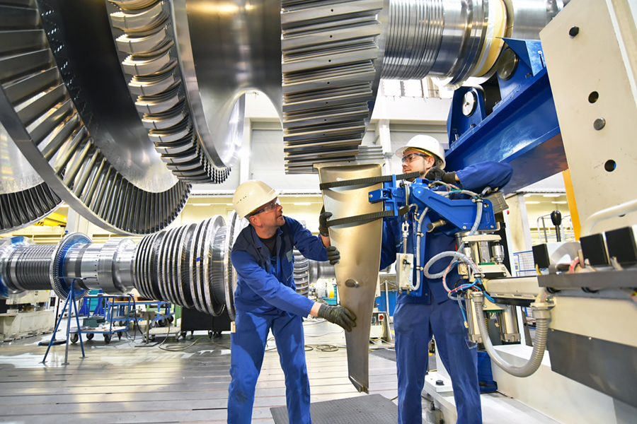 Two workers in protective gear assembling or inspecting large turbine components in an industrial facility.