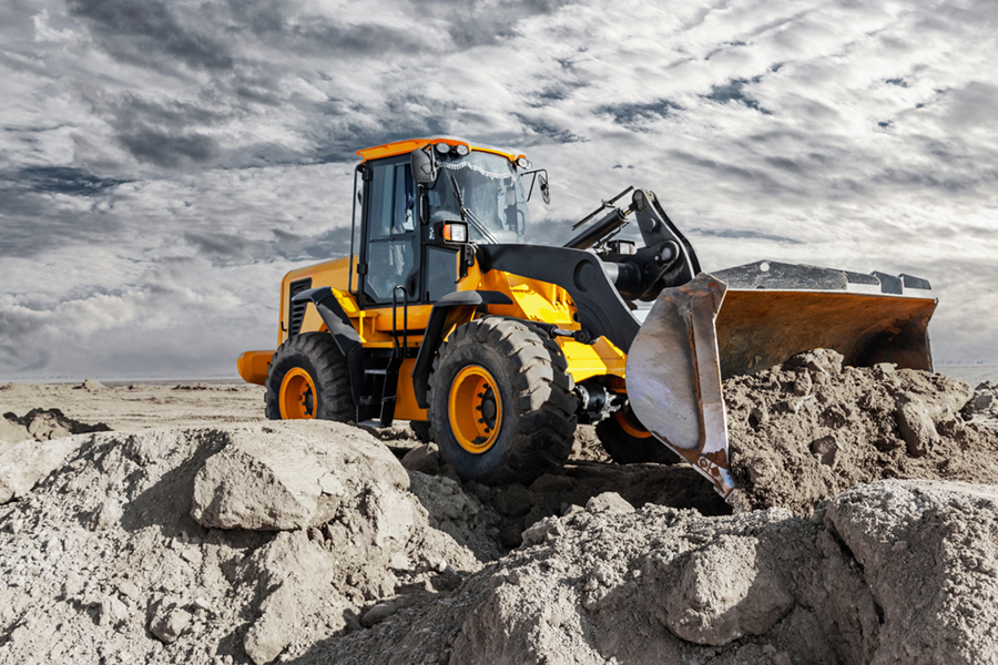 Special vehicle in action: A yellow heavy-duty front loader moves earth on a construction site under a dramatic cloudy sky.
