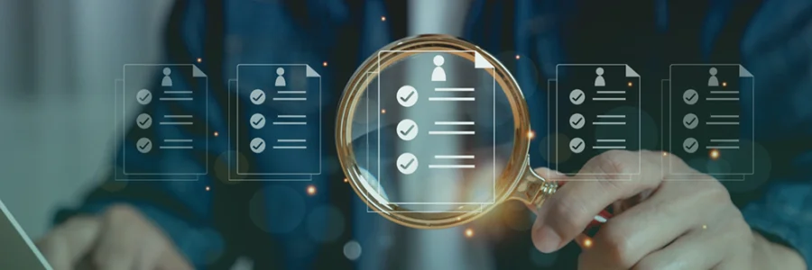 Close-up of a hand holding a magnifying glass in front of digital CV icons, with a laptop in the background, symbolizing targeted personnel placement.